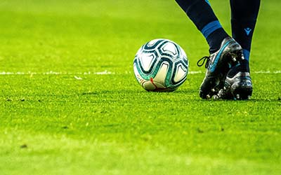 A close up shot of a football, on a pitch, about to be kicked by a player. Image by Emilio Garcia on Unsplash.