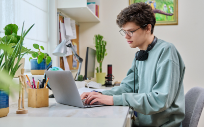 A student working at his laptop with headphones around his neck