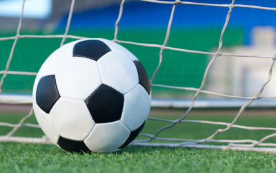 A football on a pitch, pictured against a goal net.