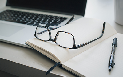 Laptop, notebook, pair of glasses, and a pen