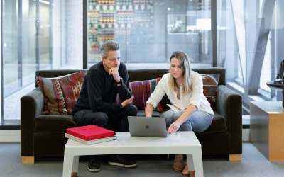 A man and a women sitting on a couch whilst looking at a laptop