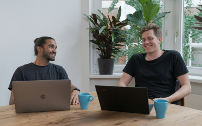 Two men are smiling at each other with their laptops during a meeting