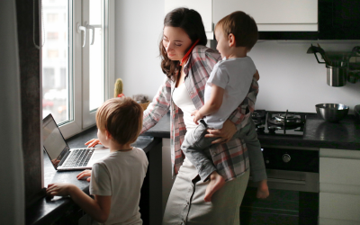 A woman with her two children, on the phone and looking at her laptop