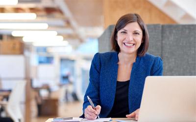 A woman seated in front of a laptop, holding a pen