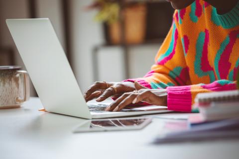 A person in a colourful jumper typing on a laptop