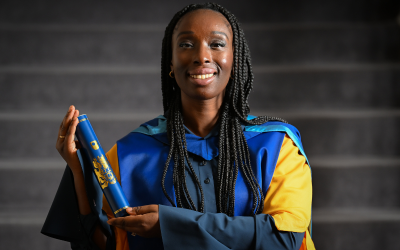 Eunice Olumide wearing an OU honorary graduate gown and holding a graduation scroll. 