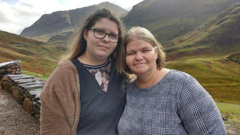Two women standing for a picture together with a green highland landscape in the background.