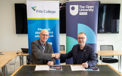 Jim Metcalfe, Fife College Principal and Chief Executive Officer, and Martin Boyle, OU in Scotland Principal, seated at a table and shaking hands with each other, while looking directly towards the camera.