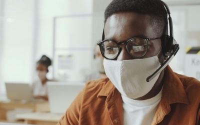 Man wearing a mask and a headset, working at a desk 