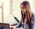 A seated smiling woman, looking at a laptop screen