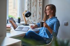 A woman with a mug in her hand, looking at a laptop