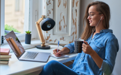 A woman watching a webinar and taking notes with a mug in her hand