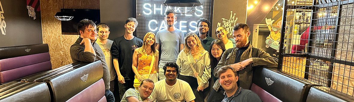 A large group in outdoor clothing stand for a photo on a bridge with trees in the background.