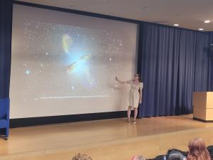 A woman presenting on a stage with an image of space behind her