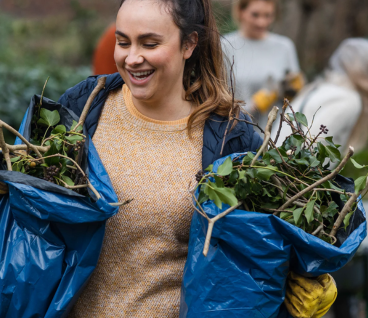 Person yn cario bagiau o ganghennau a gwastraff gardd