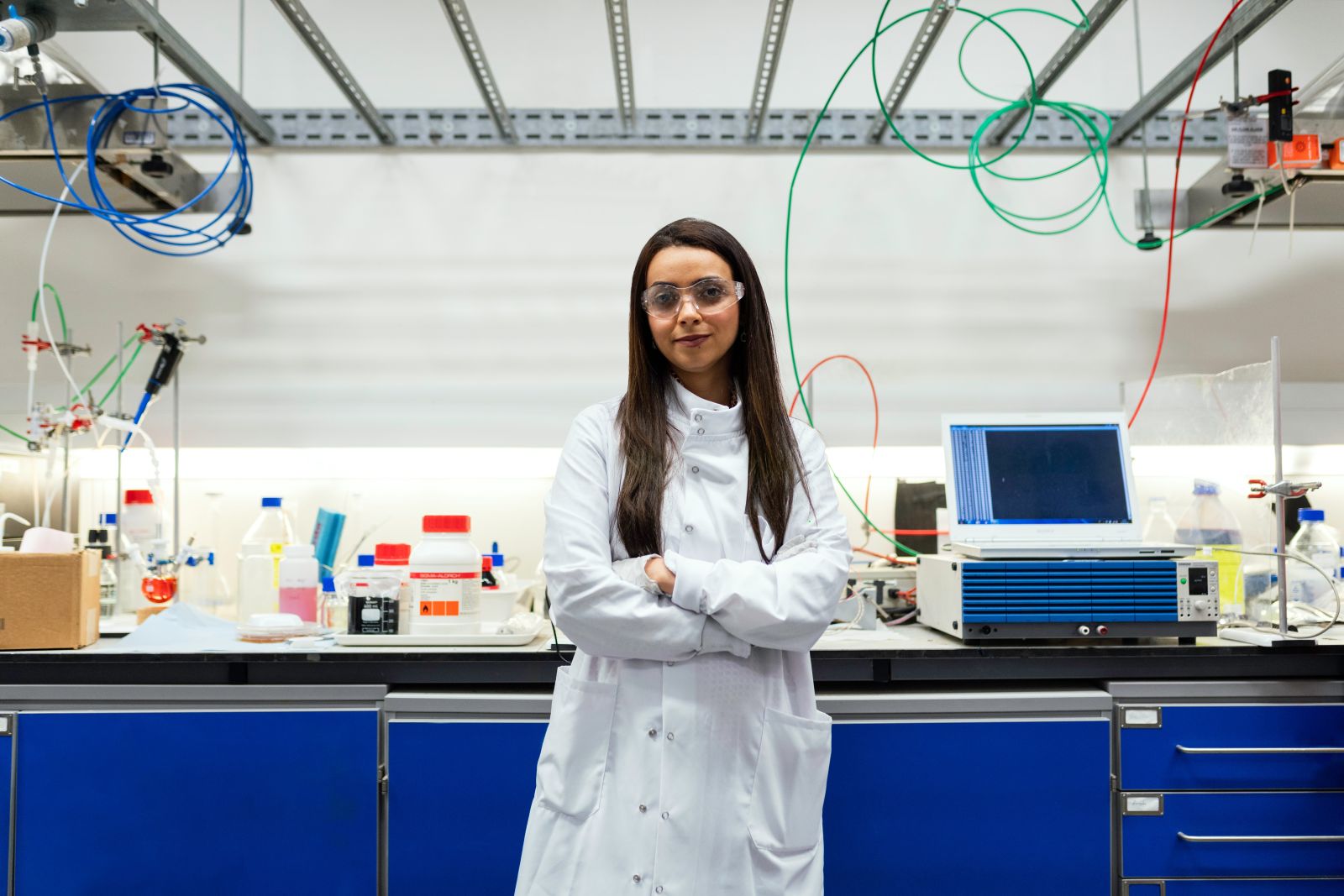 A student in a laboratory with safety goggles and a white labcoat