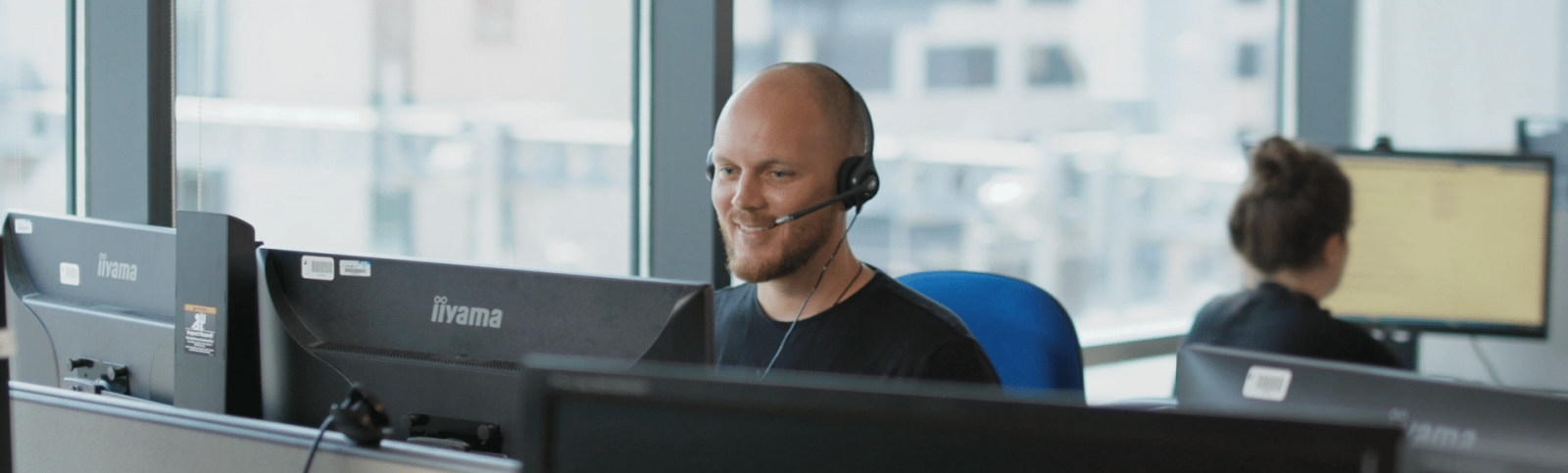 Man working on a computer wearing a headset. Dyn yn gweithio ar gyfrifiadur yn gwisgo clustffon. 