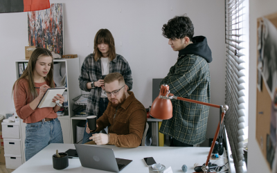 A team of four young people in a work place discuss a project around a desk