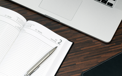 Laptop, open diary and pen on a desk